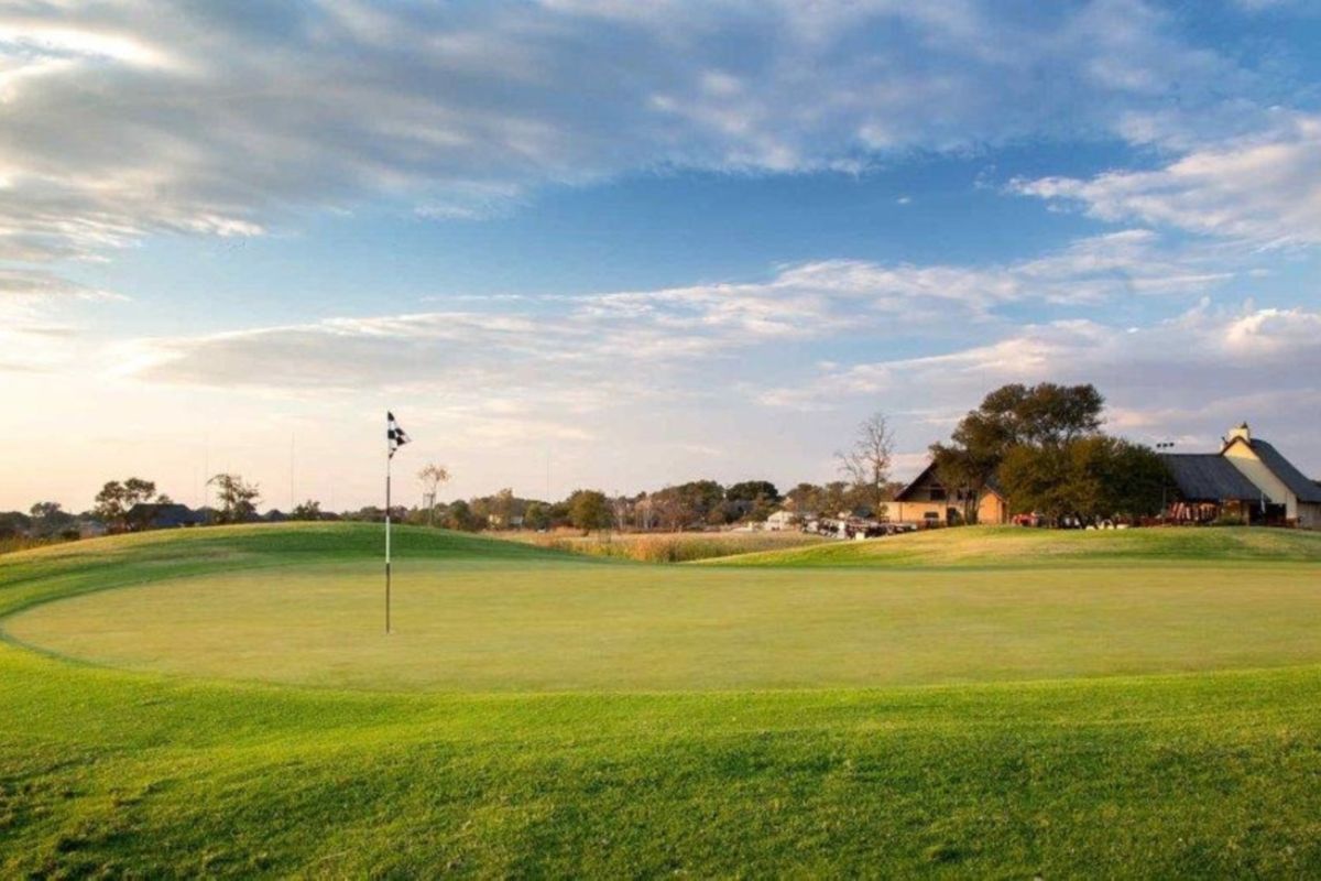 A scenic view of a well-maintained golf course green with a flag, showcasing the surrounding landscape and estate clubhouse in the distance.