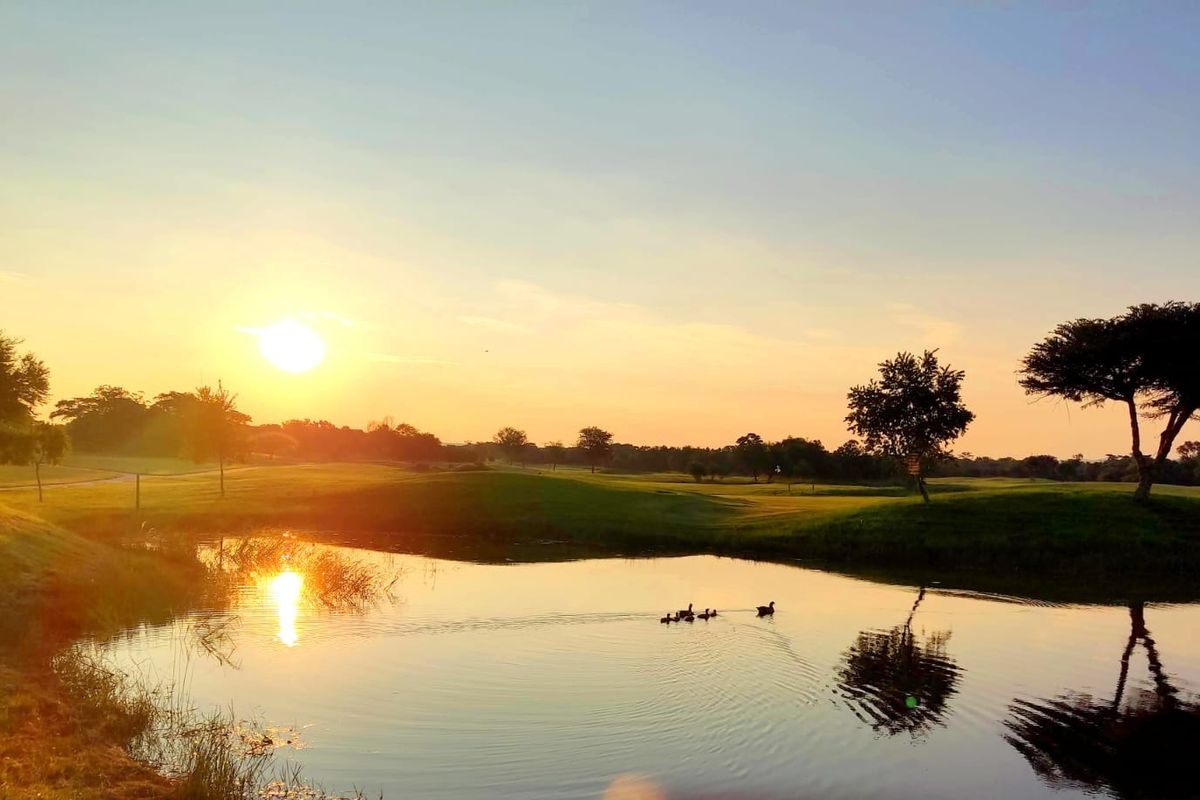 A scenic view of a tranquil pond set within a landscaped residential estate at sunset.