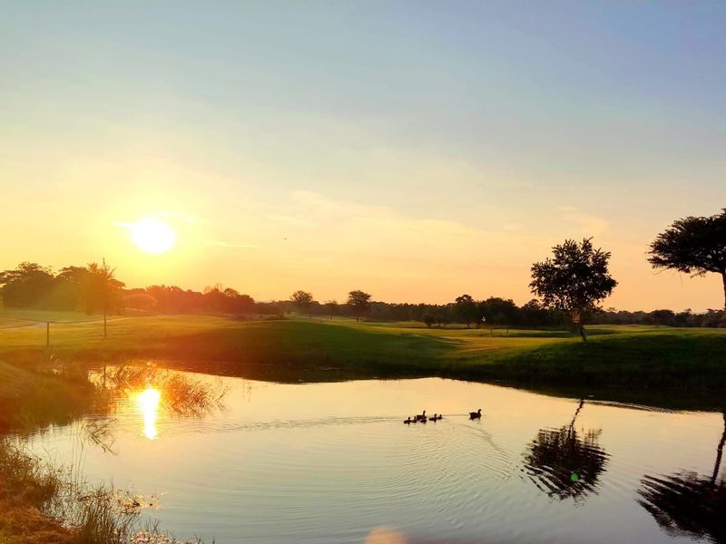 A scenic view of a tranquil pond set within a landscaped residential estate at sunset.