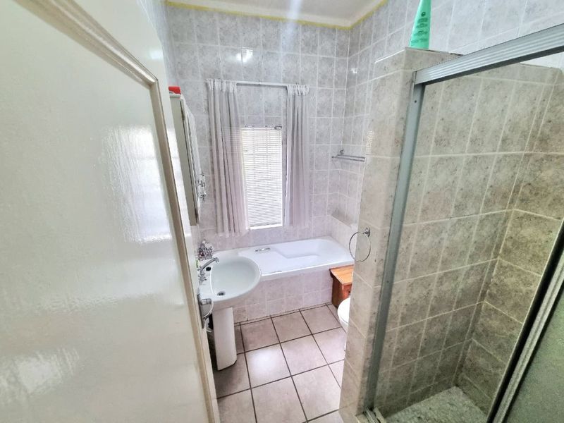 A functional bathroom featuring a pedestal basin, a built-in bathtub, and a separate shower enclosure with tiled finishes throughout.