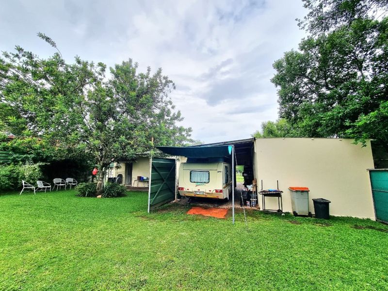 A spacious garden area featuring a well-maintained lawn, mature trees, and a functional carport structure for vehicle storage.