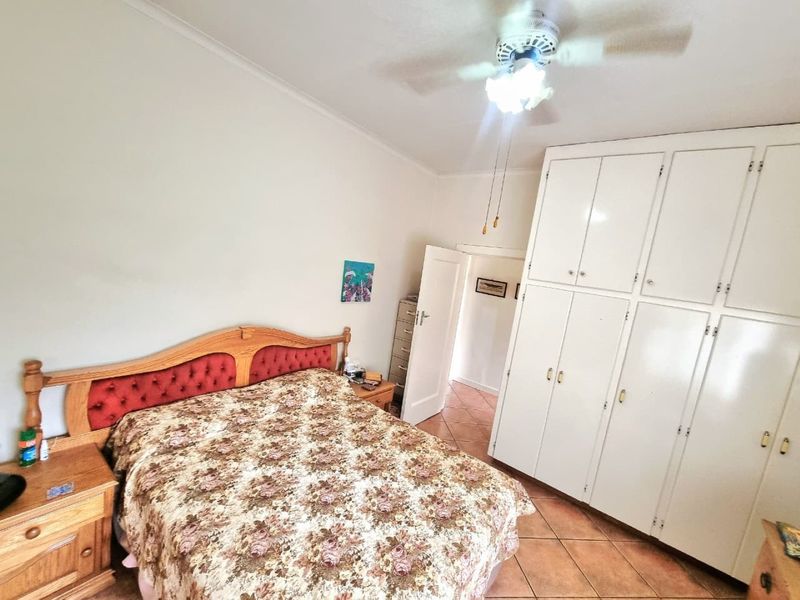 A bedroom featuring built-in cupboards, a ceiling fan, and tiled flooring, offering a functional space with potential for modern updates.