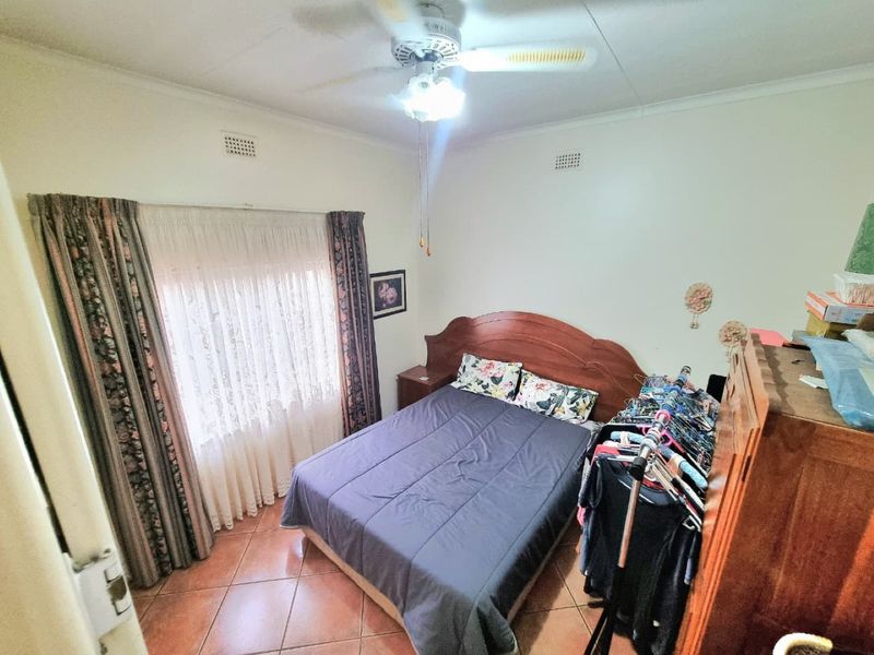 A standard bedroom featuring tiled flooring, a ceiling fan, and large windows with curtain rails.