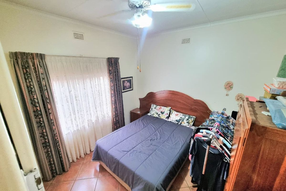A standard bedroom featuring tiled flooring, a ceiling fan, and large windows with curtain rails.