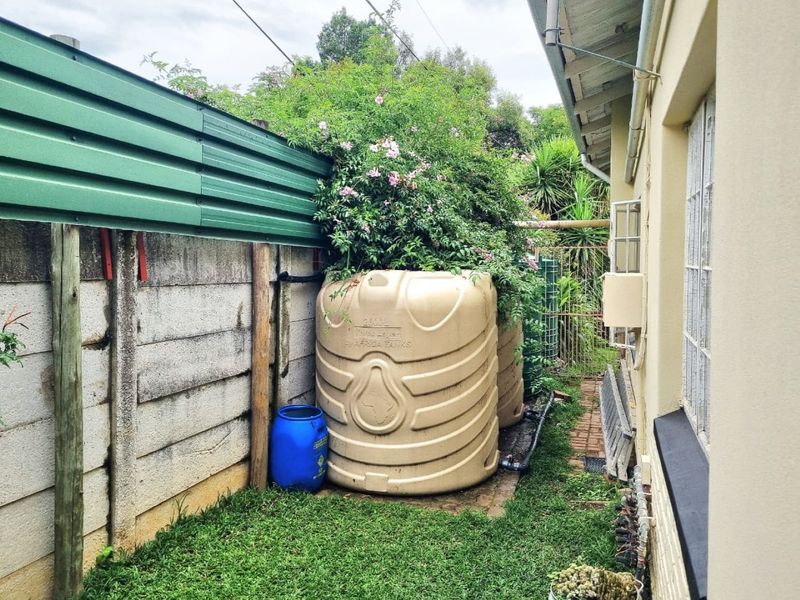 Side exterior area featuring large water storage tanks, a precast concrete boundary wall with metal extension, and brick paving along the house exterior.