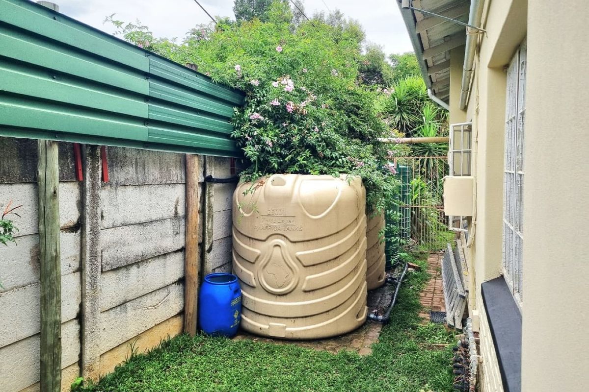 Side exterior area featuring large water storage tanks, a precast concrete boundary wall with metal extension, and brick paving along the house exterior.