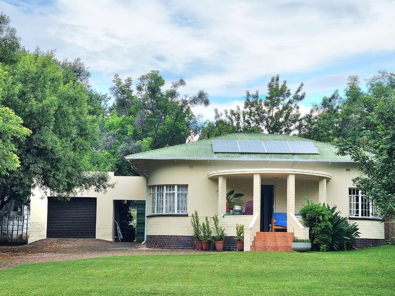 A charming single-story home featuring a covered porch, brick exterior, metal roof with solar panels, and an attached garage set on a landscaped lawn.