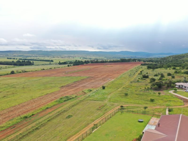 Aerial view of the expansive farm property, showcasing large open fields, surrounding landscape, and the main dwelling with a metal roof.
