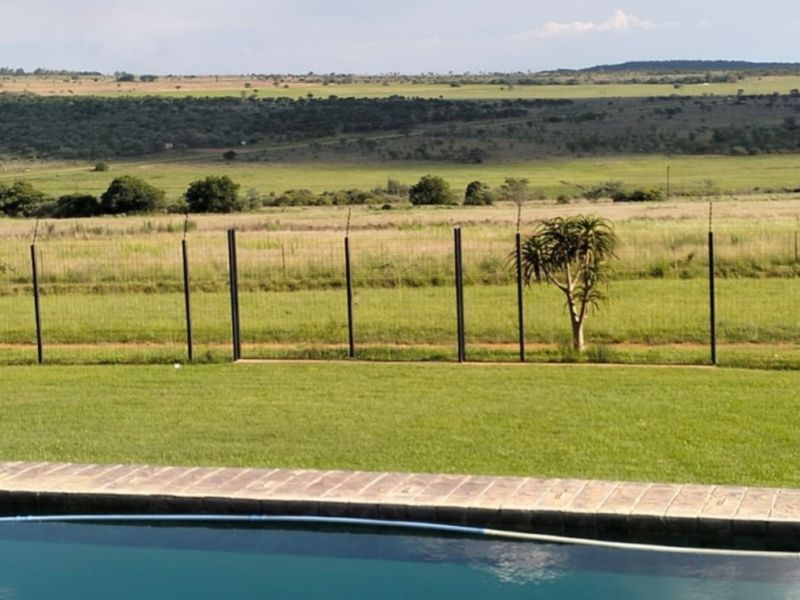 A well-maintained swimming pool area featuring paved coping, overlooking an expansive rural landscape enclosed by a wire mesh and electric perimeter fence.
