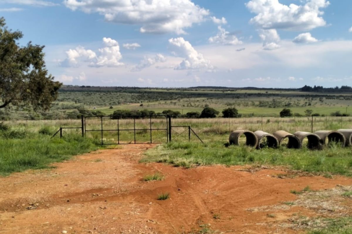 A view of a farm property featuring a metal barn structure, a gated entrance, and open grazing land under a clear sky.