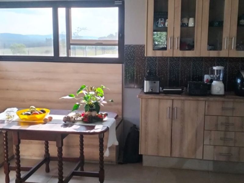 A functional kitchen featuring light wood-finish cabinetry, a decorative tiled backsplash, and large windows offering scenic views of the surrounding farm landscape.