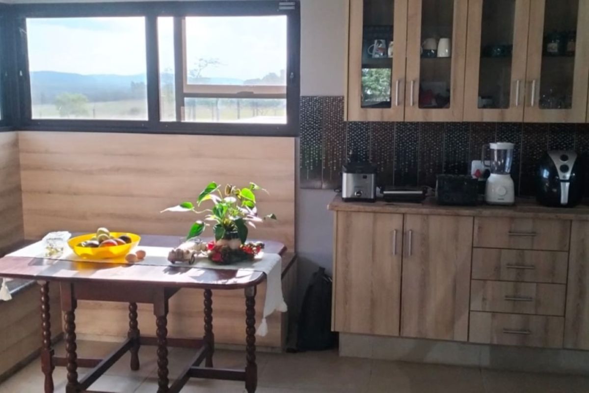 A functional kitchen featuring light wood-finish cabinetry, a decorative tiled backsplash, and large windows offering scenic views of the surrounding farm landscape.