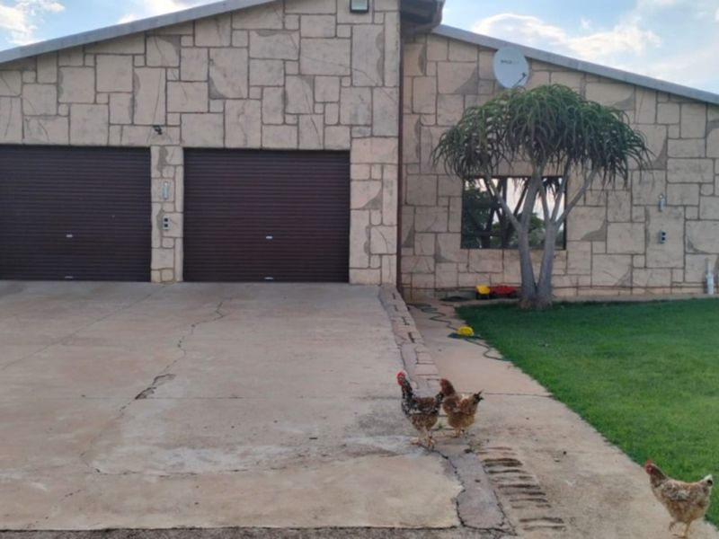 Front view of a farm property featuring a double garage with roller doors and stone cladding facade, set on a large lawn area.