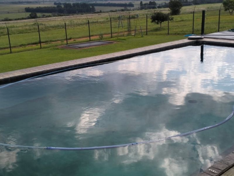 Outdoor swimming pool area featuring a paved surround and perimeter fencing, overlooking expansive rural farm landscape views.
