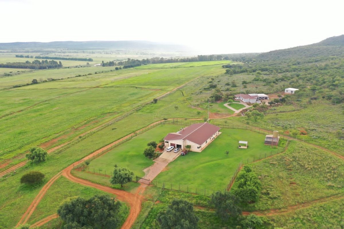 Aerial view of a farm property featuring a main residence, outbuildings, fenced grounds, and expansive surrounding agricultural land.