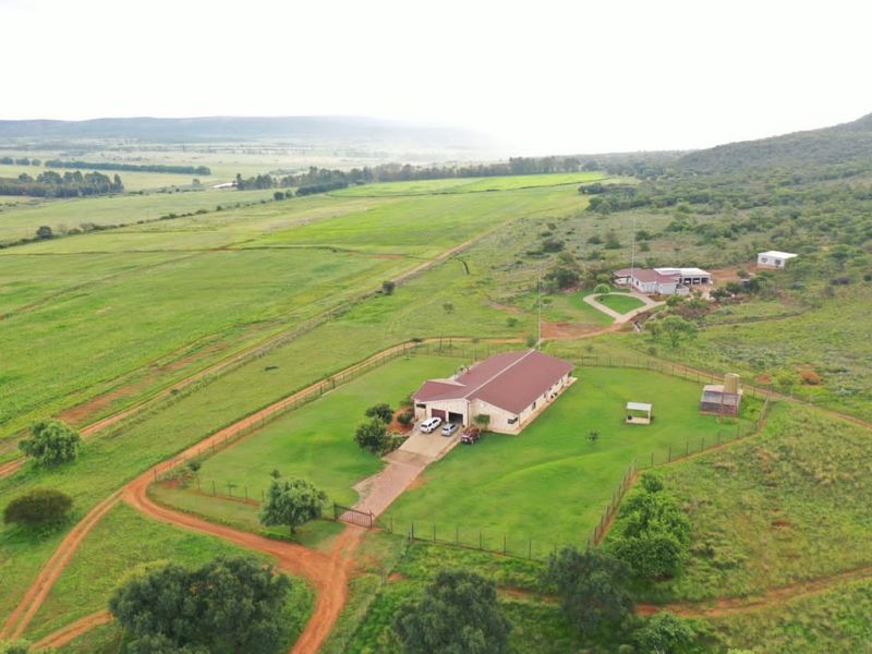 Aerial view of a farm property featuring a main residence, outbuildings, fenced grounds, and expansive surrounding agricultural land.