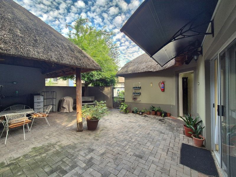 A paved outdoor patio area featuring a thatched roof structure, sliding glass door access, and a protective awning.