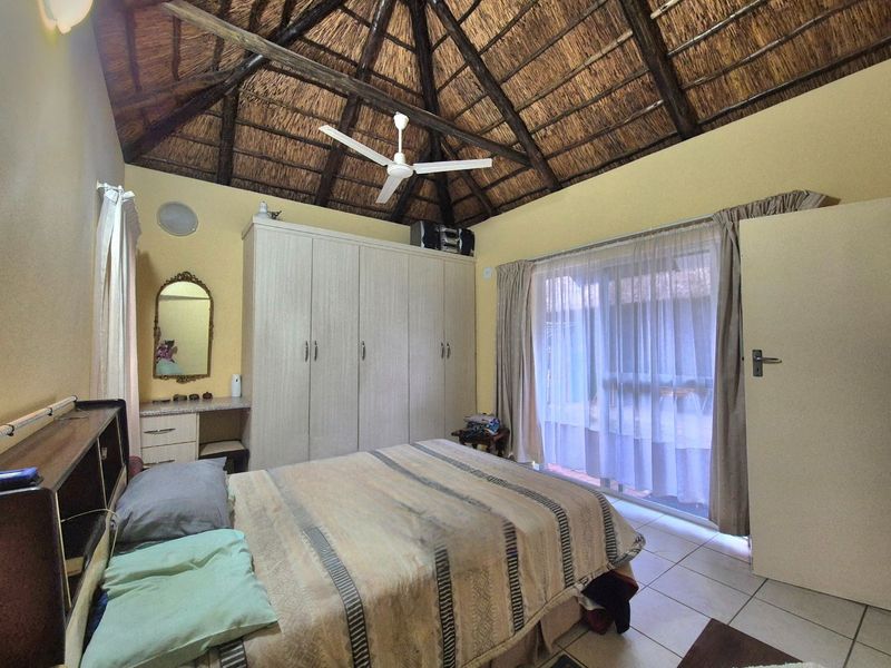 A bedroom featuring a high thatched ceiling with exposed timber rafters, built-in cupboards, tiled flooring, and a sliding glass door leading outside.