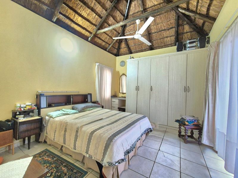Spacious bedroom featuring a high thatched ceiling with exposed timber rafters, tiled flooring, and ample built-in wardrobe storage.