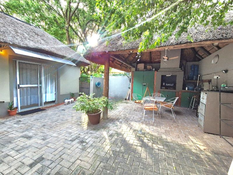 Covered outdoor patio area featuring a built-in braai, brick paving, and a traditional thatched roof, providing a rustic space for outdoor entertaining.
