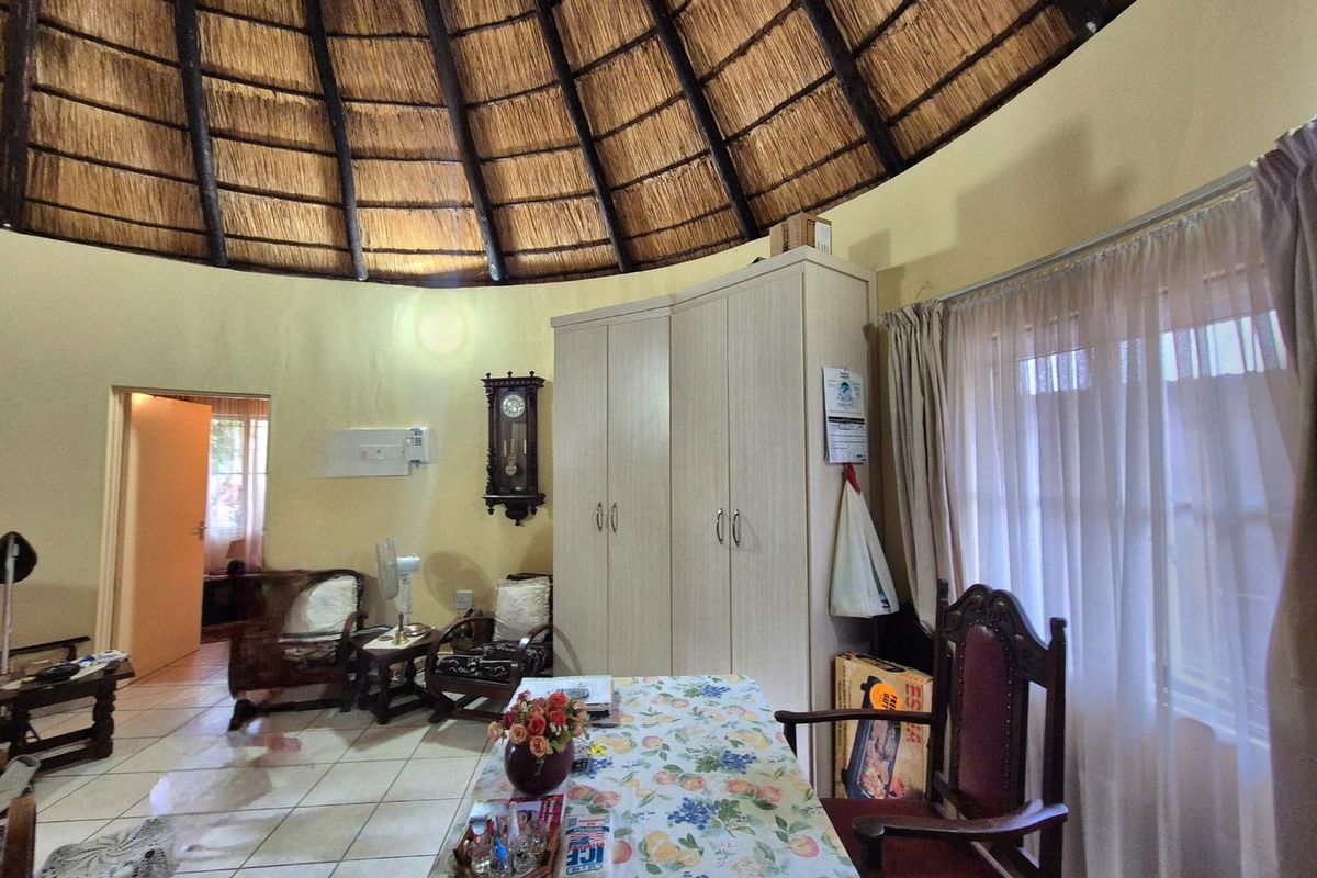 A bedroom featuring a unique circular layout with a high thatched roof, exposed timber rafters, tiled flooring, and a built-in wardrobe.