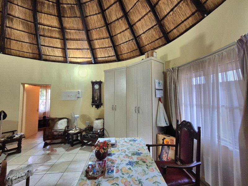 A bedroom featuring a unique circular layout with a high thatched roof, exposed timber rafters, tiled flooring, and a built-in wardrobe.