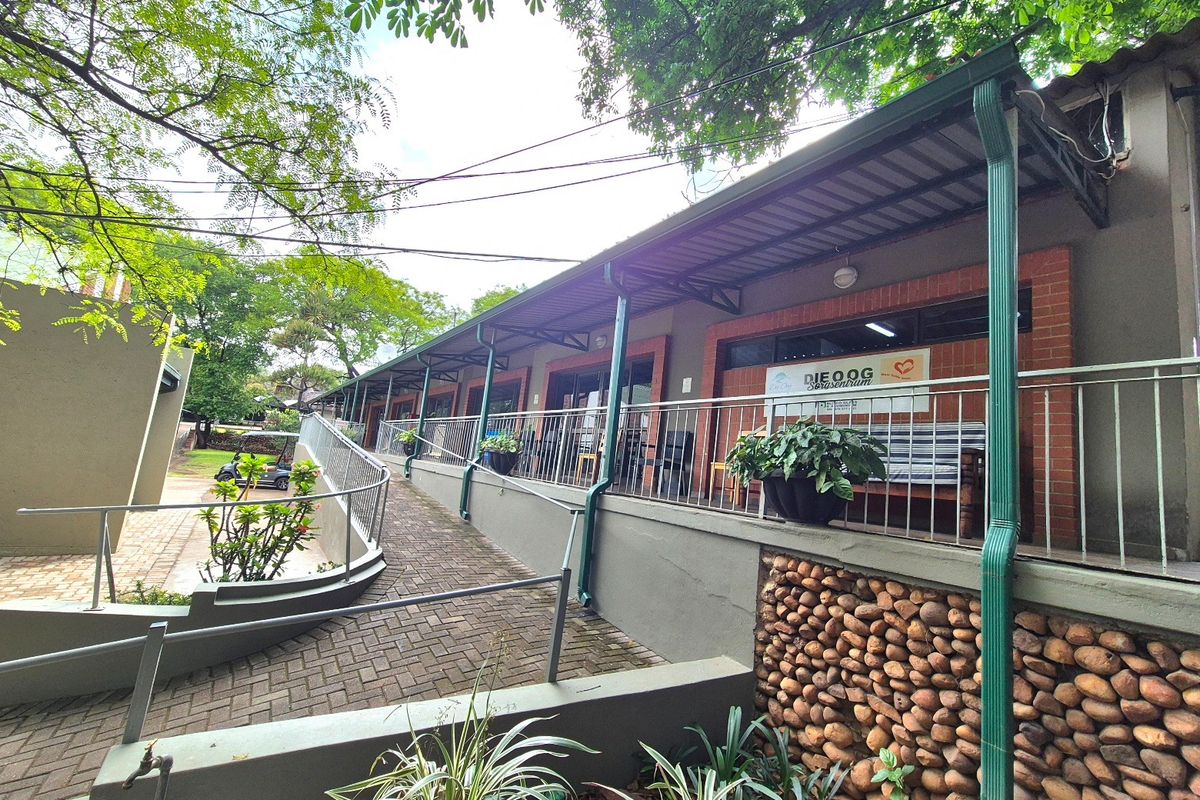 Exterior view of a building featuring a paved accessibility ramp, metal handrails, and a covered patio area with brick and stone architectural details.