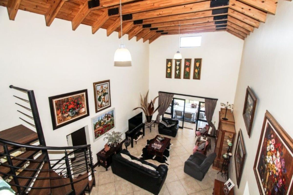 Spacious living room featuring a high vaulted ceiling with exposed timber rafters, tiled flooring, and a spiral staircase leading to an upper level.