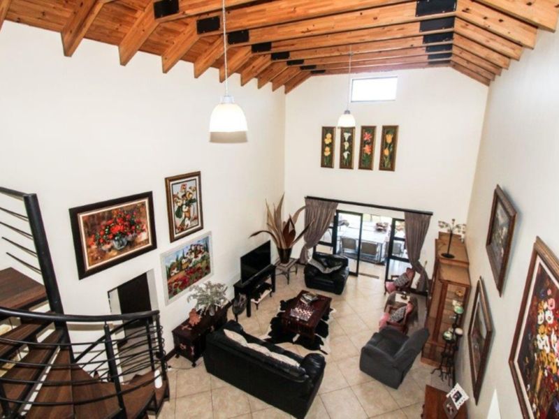 Spacious living room featuring a high vaulted ceiling with exposed timber rafters, tiled flooring, and a spiral staircase leading to an upper level.