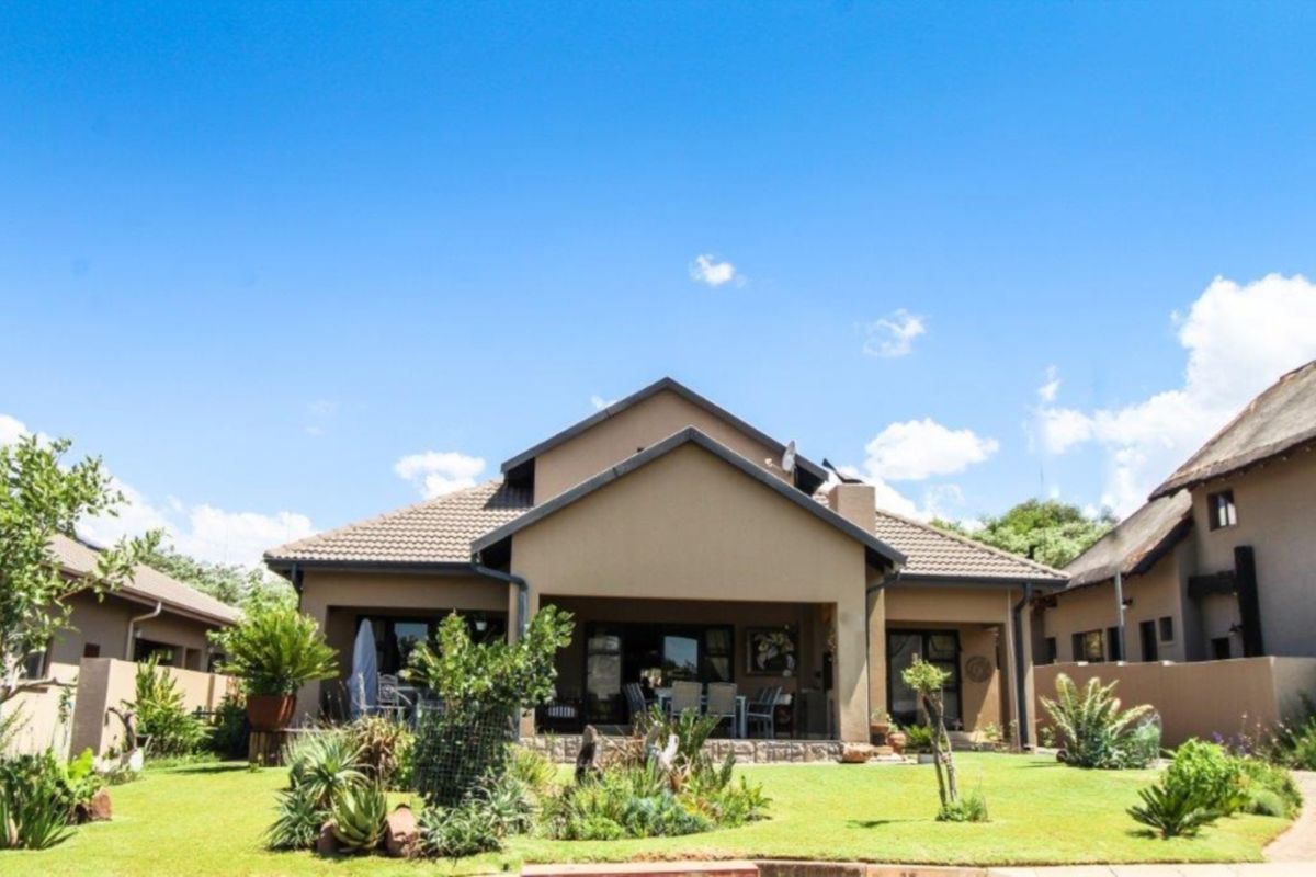 Rear view of the house featuring a covered patio, tiled roof, and a well-maintained landscaped garden.