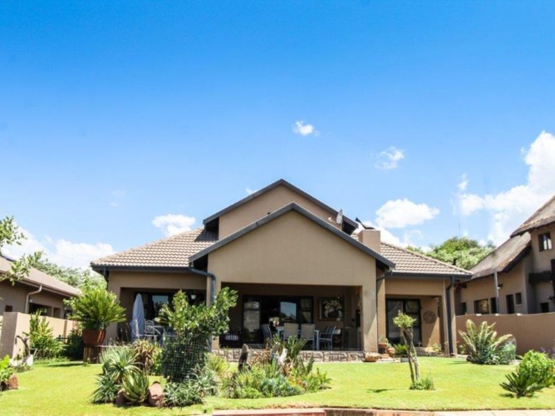 Rear view of the house featuring a covered patio, tiled roof, and a well-maintained landscaped garden.