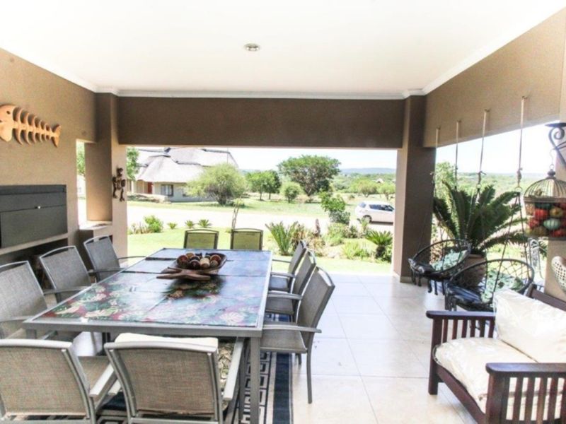A spacious covered patio featuring a built-in braai, tiled flooring, and open views of the surrounding landscape, ideal for outdoor dining and relaxation.