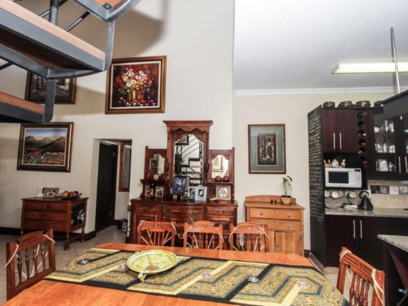 Open-plan living and dining area featuring high ceilings, tiled flooring, a staircase, and built-in kitchen cabinetry with granite countertops.