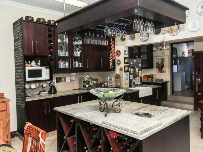 A well-appointed kitchen featuring dark wood cabinetry, granite countertops, a central island with integrated wine storage, and a classic farmhouse sink.
