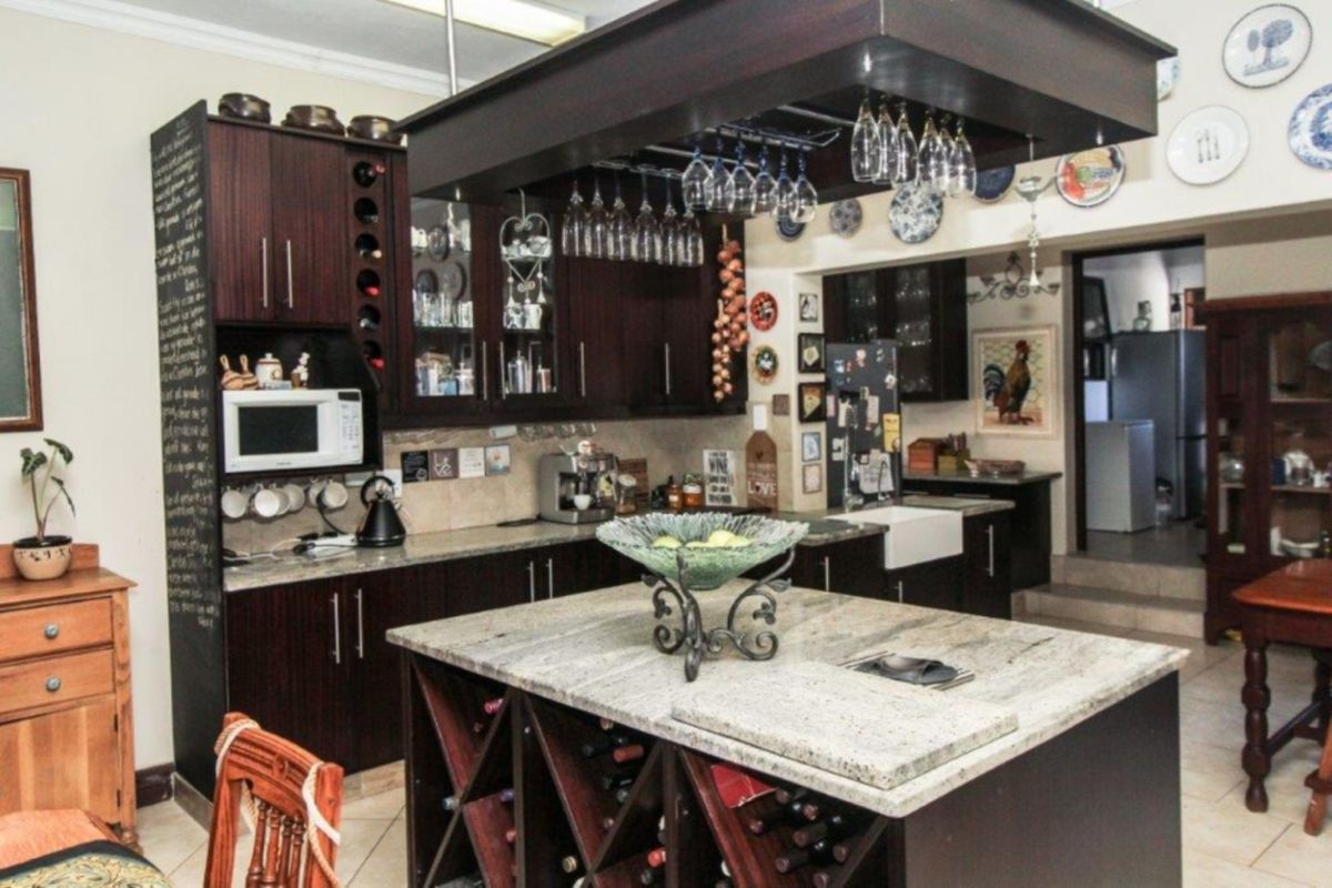 A well-appointed kitchen featuring dark wood cabinetry, granite countertops, a central island with integrated wine storage, and a classic farmhouse sink.