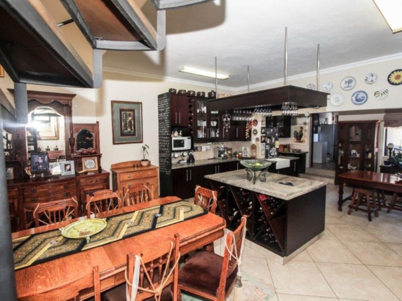 Spacious open-plan kitchen and dining area featuring dark wood cabinetry, a central stone-topped island with integrated wine storage, and ceramic tile flooring.