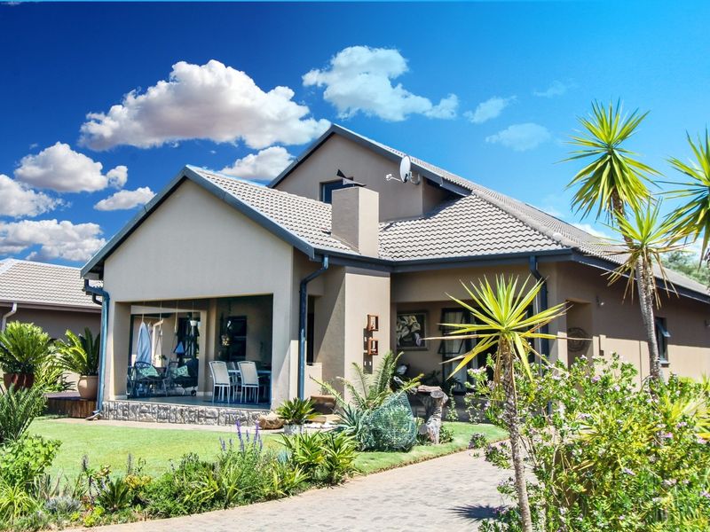A well-maintained residential property featuring a tiled roof, stone-clad accents, and a spacious covered patio overlooking a landscaped garden and paved walkway.