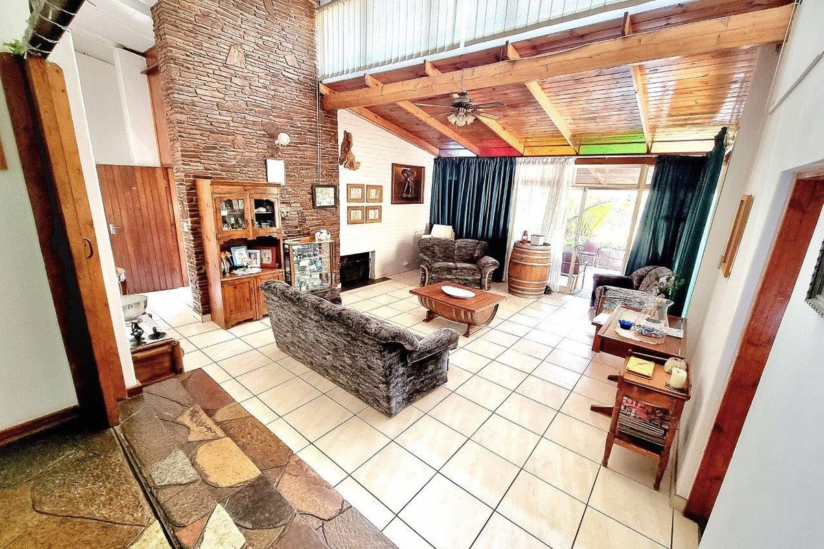 Spacious living room featuring a prominent stone fireplace, exposed timber ceiling beams, and large sliding glass doors leading to the outdoor area.