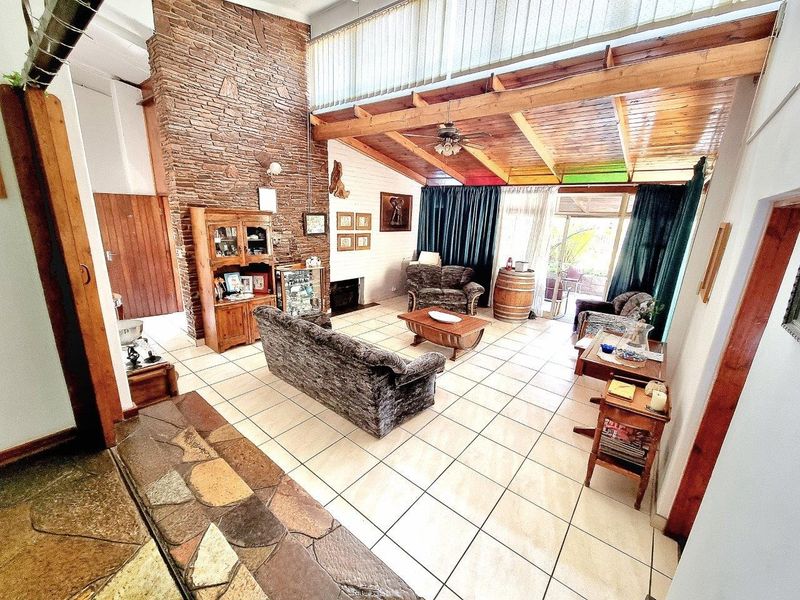 Spacious living room featuring a prominent stone fireplace, exposed timber ceiling beams, and large sliding glass doors leading to the outdoor area.