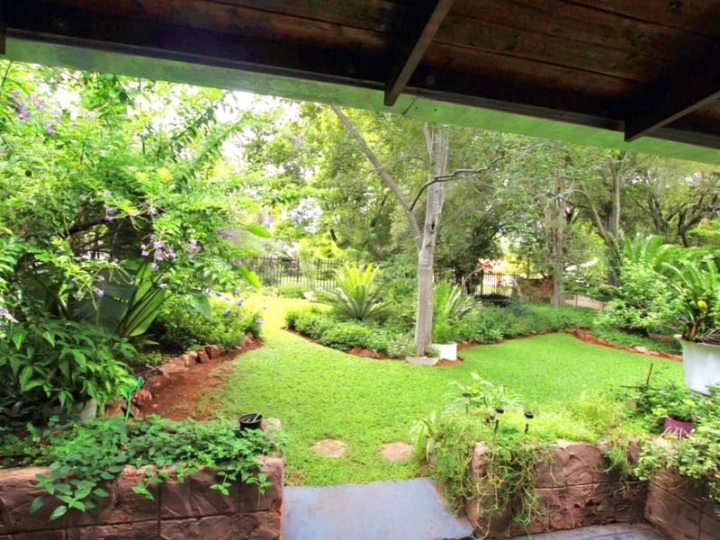 A covered patio area overlooking a lush, well-maintained garden with stone retaining walls and mature trees.