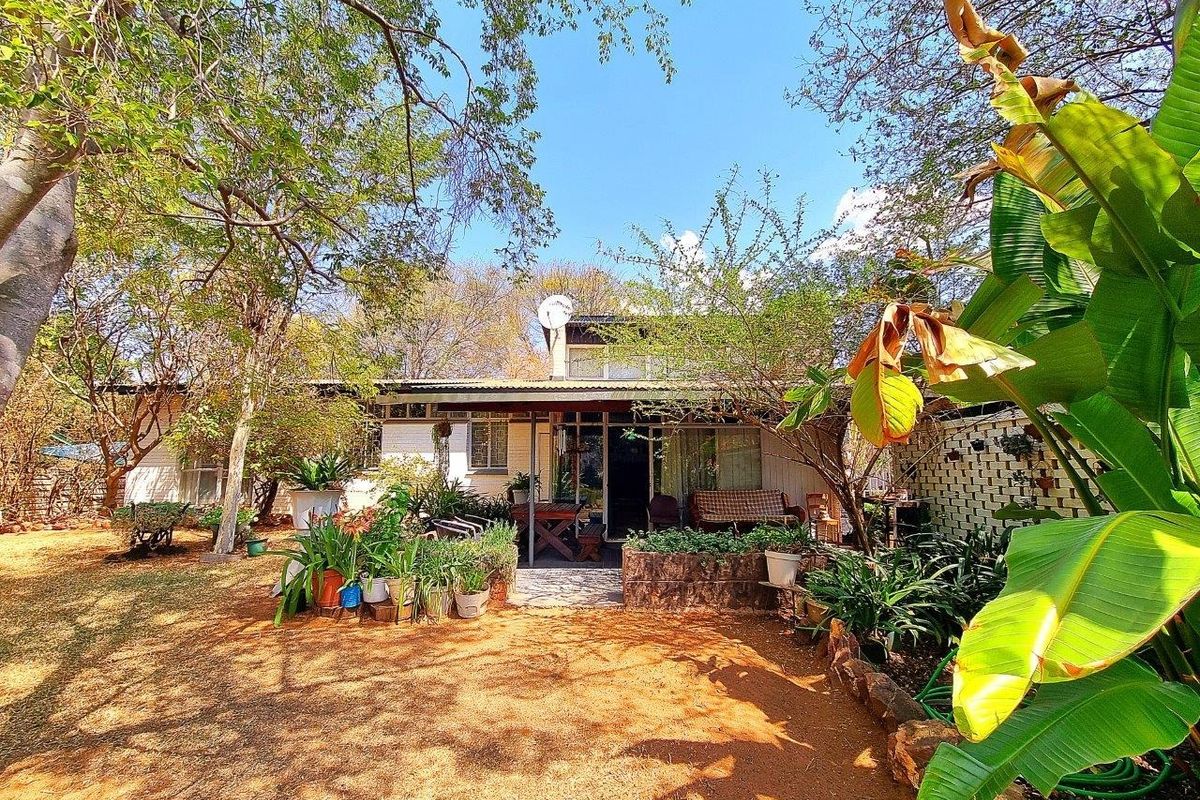 Rear view of the property featuring a covered patio area, brick retaining wall, and established garden surroundings.