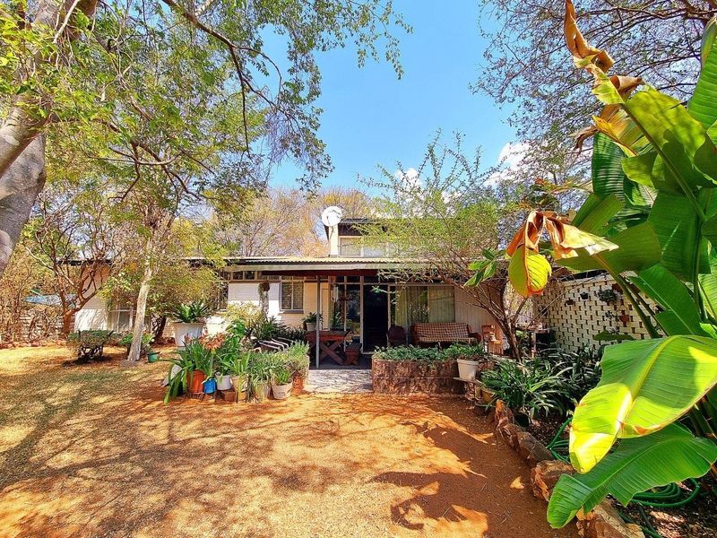 Rear view of the property featuring a covered patio area, brick retaining wall, and established garden surroundings.