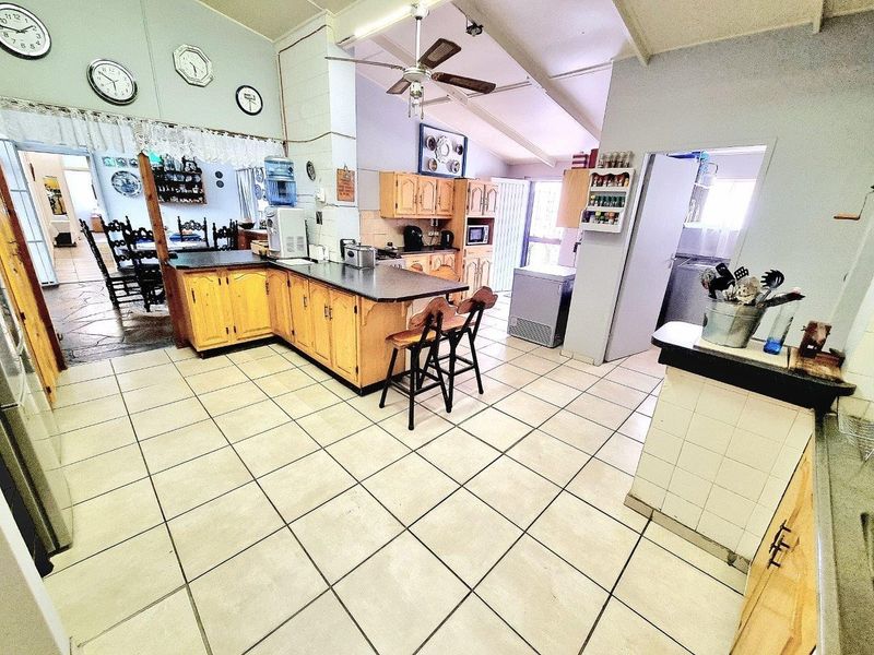 Spacious kitchen featuring wooden cabinetry, laminate countertops, and tiled flooring under a vaulted ceiling, offering a functional layout with potential for modern updates.