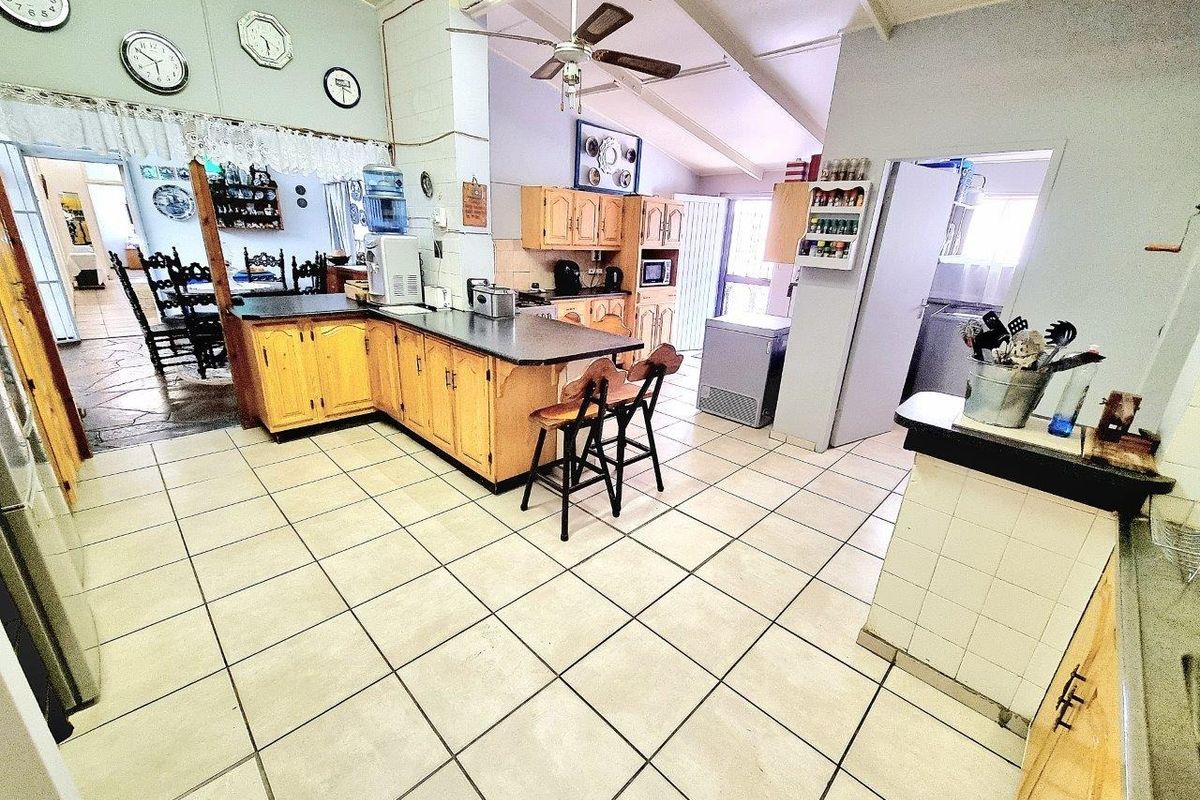 Spacious kitchen featuring wooden cabinetry, laminate countertops, and tiled flooring under a vaulted ceiling, offering a functional layout with potential for modern updates.