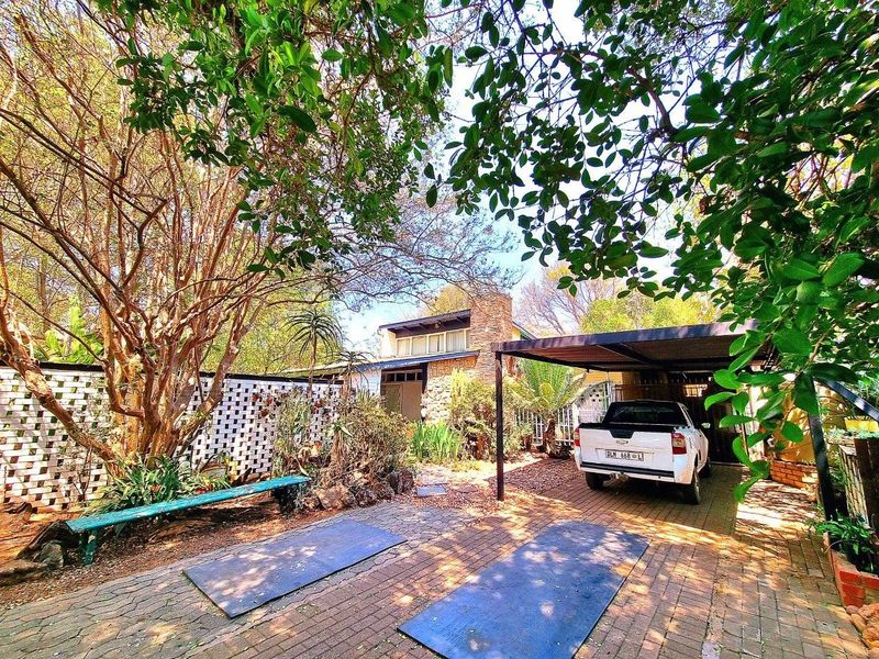 Front exterior view of the house featuring a paved driveway, a covered carport, and established garden landscaping with mature trees.