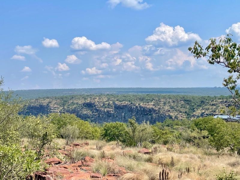 A scenic view overlooking a natural rocky escarpment and expansive native bushveld landscape.