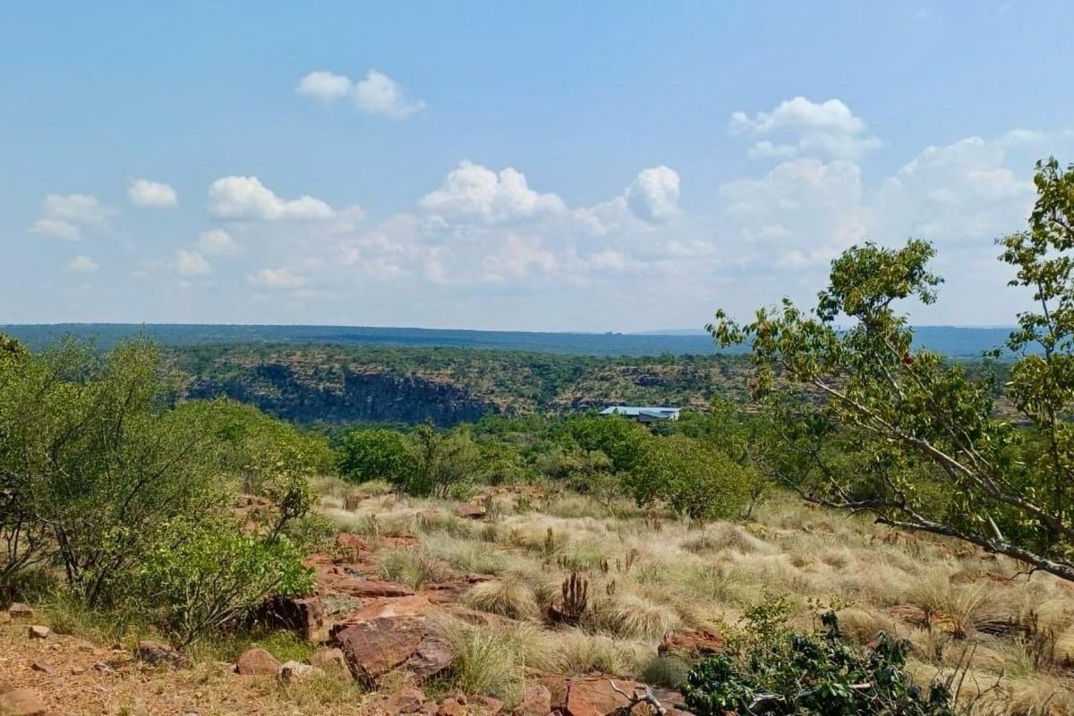 A scenic, elevated landscape view overlooking natural bushveld, rocky terrain, and distant hills, showcasing the expansive natural surroundings of the vacant land.