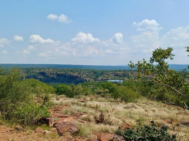 A scenic, elevated landscape view overlooking natural bushveld, rocky terrain, and distant hills, showcasing the expansive natural surroundings of the vacant land.