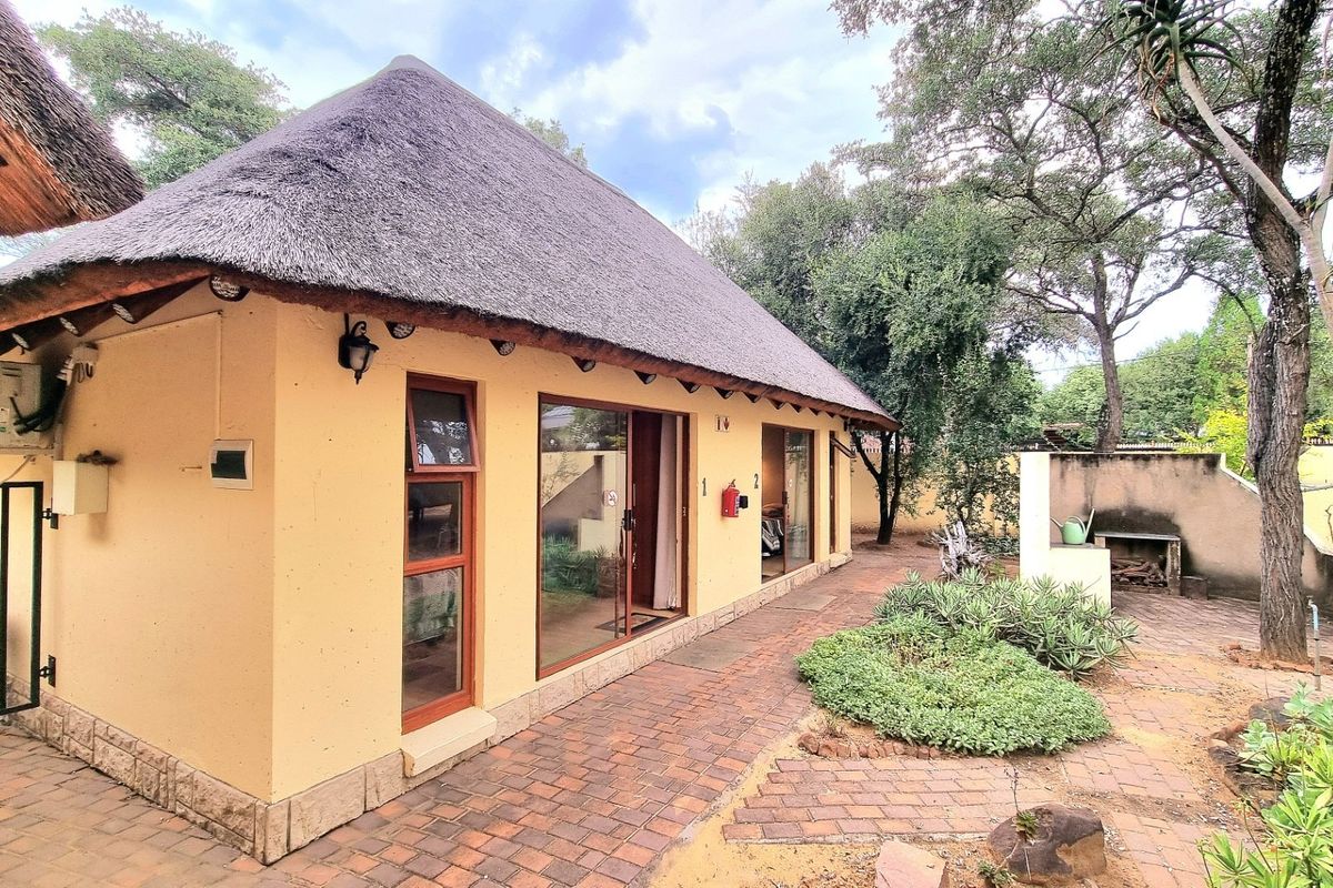 Rear view of a thatched-roof dwelling featuring sliding glass doors, brick-paved patio area, and a built-in outdoor braai facility.
