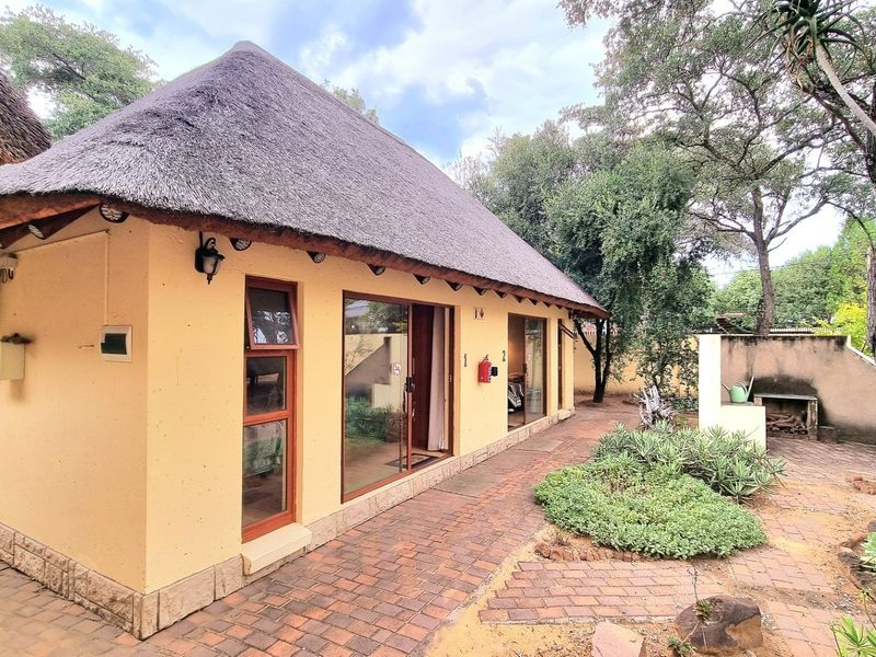 Rear view of a thatched-roof dwelling featuring sliding glass doors, brick-paved patio area, and a built-in outdoor braai facility.